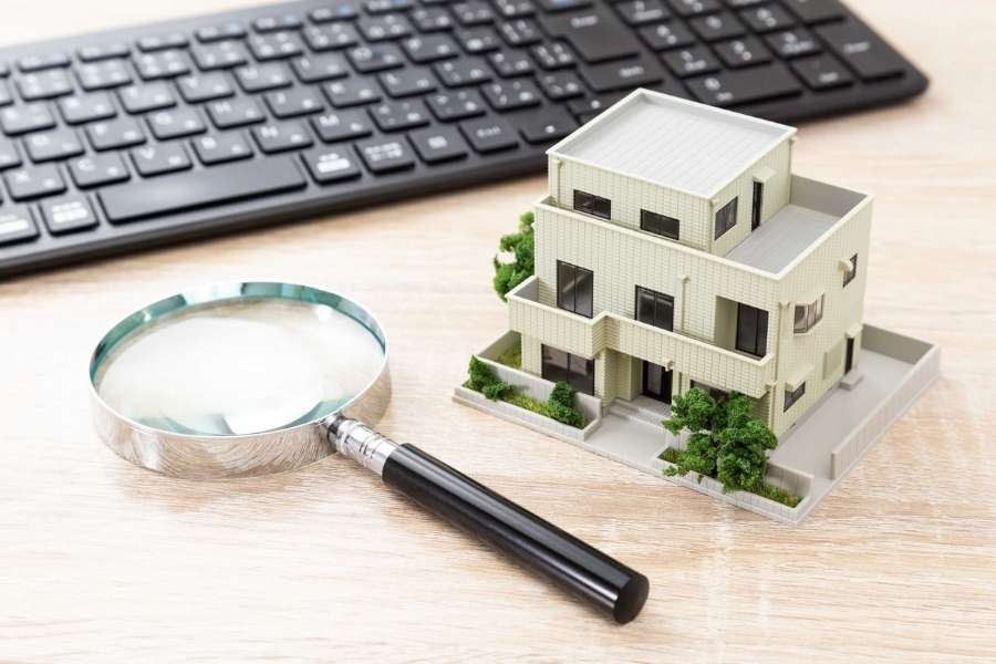 Une loupe posée à côté d'une maquette de maison et d'un clavier pour dénicher des pépites immobilières.