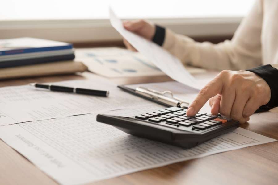 Une personne utilise une calculatrice et analyse des documents administratifs pour préparer un transfert de compte bancaire.