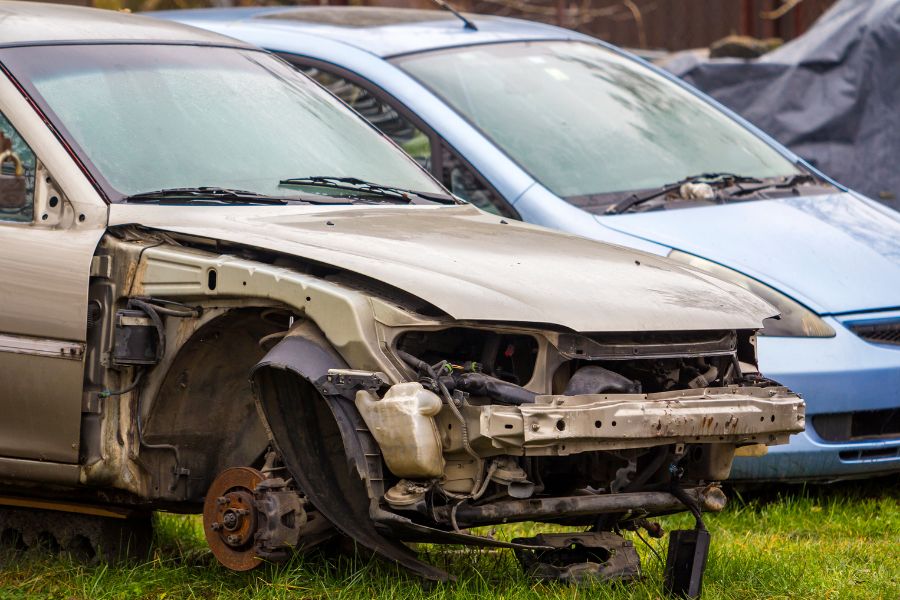 Une épave de voiture sans roue avant ni pare-chocs dans un herbage, illustrant une voiture déclarée économiquement irréparable.